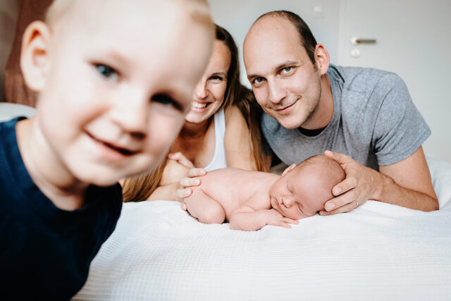 veselá fotka chlapce koukajícího do objektivu fotografa na rodinném focení s novorozencem