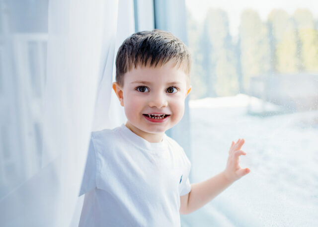 přirozená portrétní fotka chlapce v závěsu u okna