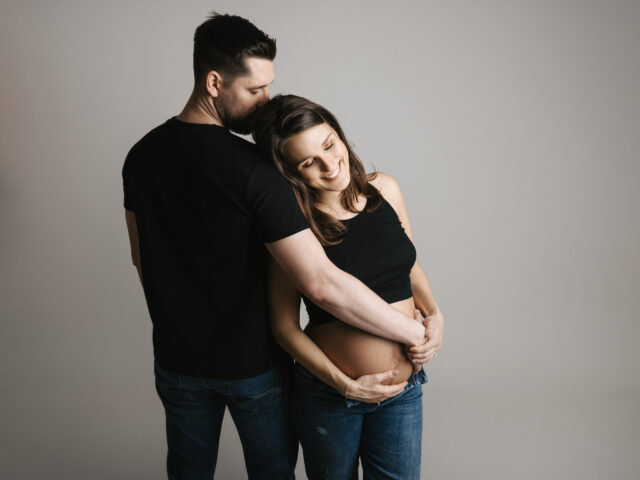 fotka z párového těhotenského focení na šedém plátně ve fotoateliéru