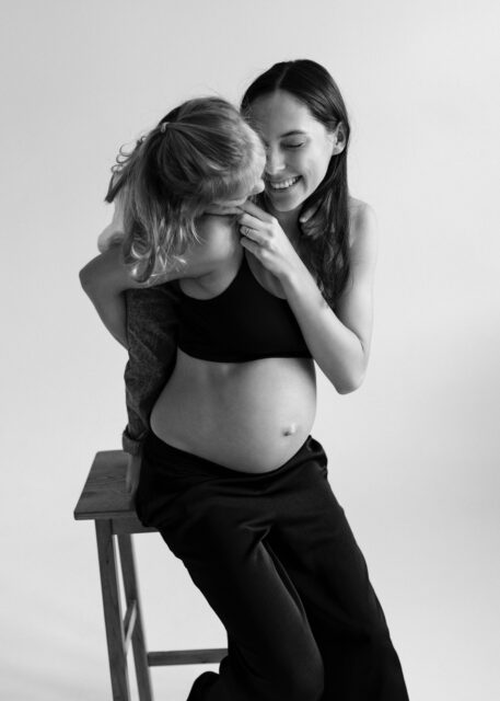 černobílá fotografie těhotné maminky v objetí se starší dcerkou na těhotenském focení v ateliéru v Praze